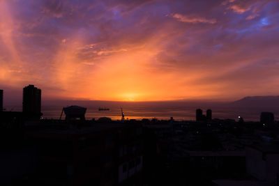 Silhouette city by sea against sky during sunset