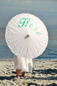 Low section of woman with umbrella standing at beach