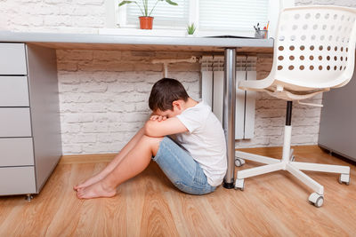 Side view of woman sitting on hardwood floor at home