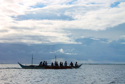 Silhouette people on boat in sea against cloudy sky