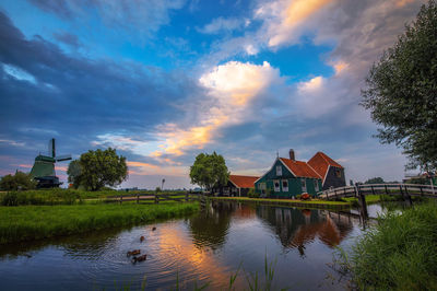 Scenic view of lake by buildings against sky during sunset