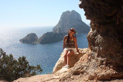 Young woman standing on rock by sea against sky