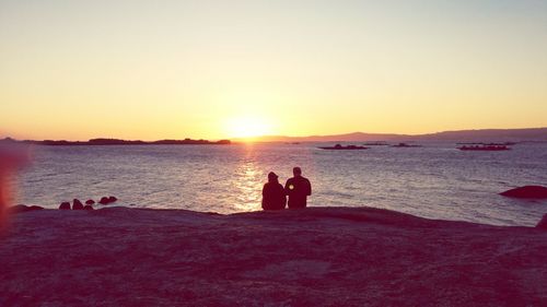 Silhouette people standing on beach against clear sky during sunset