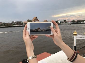 Midsection of woman photographing sea against sky