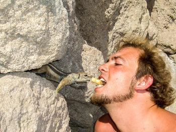 Man holding peanut in mouth while feeding chipmunk