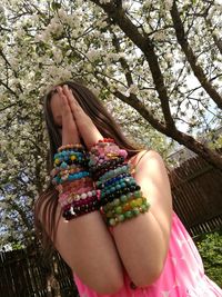 Girl with hands clasped wearing bracelets against trees