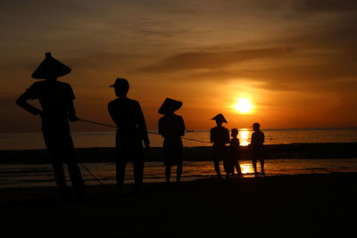 Silhouette fishermen on beach against sky during sunset