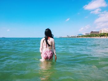 Rear view of woman wading in sea against sky