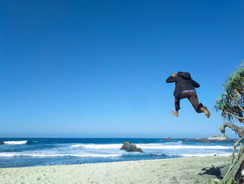 Man jumping at beach against clear sky