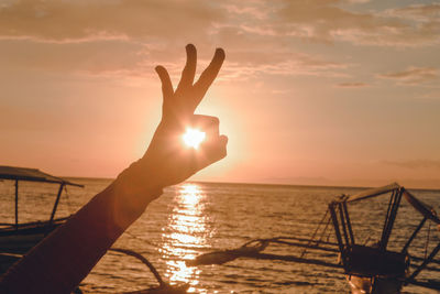 Cropped image of hand gesturing against sea during sunset