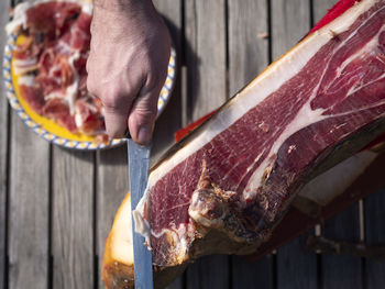 High angle view of man hand cutting a slice of dried spanish jamon serrano on wood table.