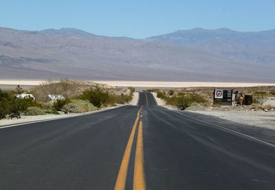 Country road leading towards mountains against sky