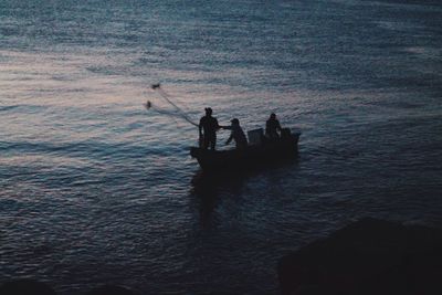 Silhouette men fishing in sea during sunset