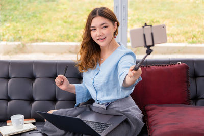 Young woman using phone while sitting on sofa