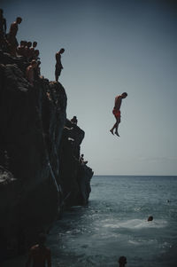 People jumping on rock by sea against sky