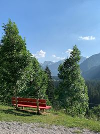 Park bench by trees against sky