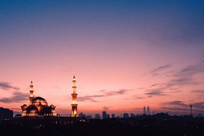 Mosque lit up at dusk against cloudy sky