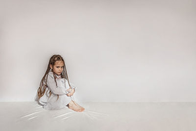 Full length of girl sitting on white wall