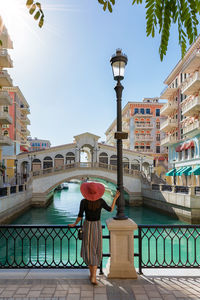 Rear view of woman by railing against canal amidst building in city