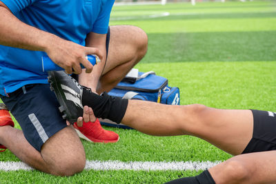 Low section of male physical therapist spraying on soccer player leg at field