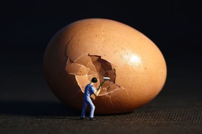 Optical illusion of figurine breaking egg against black background