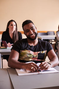 Confident student smiling while sitting at desk in language school