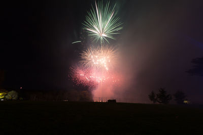 Fireworks explode in the sky with green and red colours through the smokey haze.