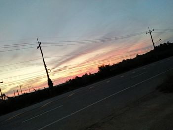 Silhouette electricity pylons against sky at sunset