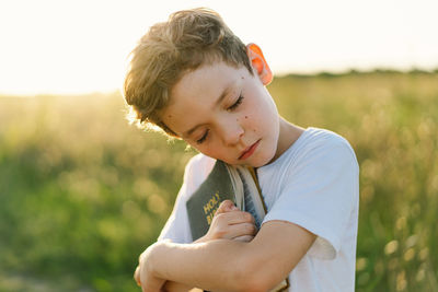 Christian boy holds bible in her hands. reading the holy bible in a field during beautiful sunset