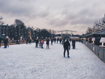 People roller skating on snowy field against cloudy sky