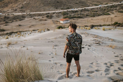 Young man looking away while standing on sand at almeria, tabernas desert, spain