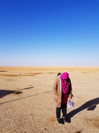 Rear view of woman standing on desert against clear sky