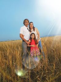 Portrait of happy family standing on grassy field against sky during sunny day