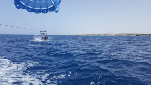 Low angle view of people paragliding over sea against clear blue sky