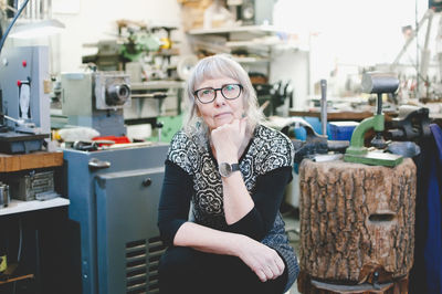 Thoughtful senior woman with hand on chin in jewelry workshop