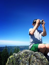 Boy photographing on mountains against clear sky