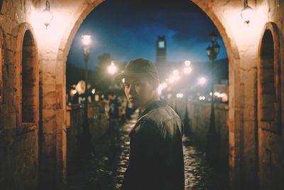 Side view of young man looking away at illuminated building