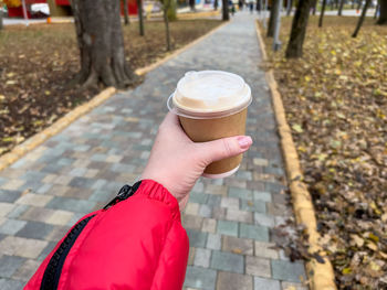Hand holding coffee cup on autumn park background