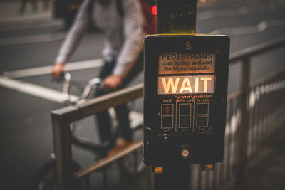 Close-up of road sign against man riding bicycle on city street