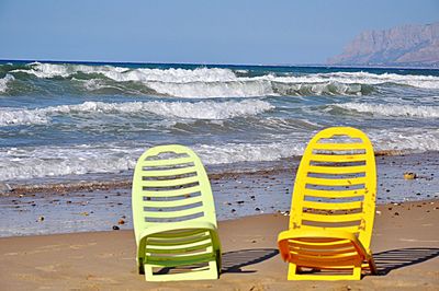 Yellow deck chairs on beach against clear sky