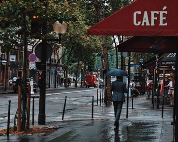 Rear view of businessman with umbrella walking on sidewalk in city during monsoon