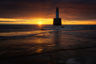 Lighthouse by sea against sky during sunset