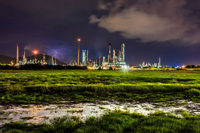 Illuminated factory by field against sky