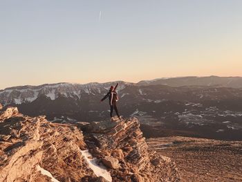 Woman standing on rock formation against sky during sunset