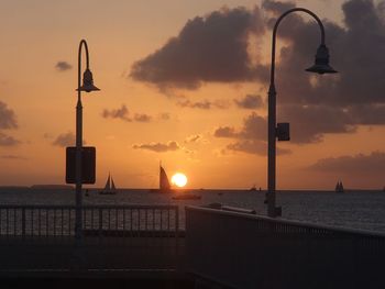 Street light by sea against sky during sunset