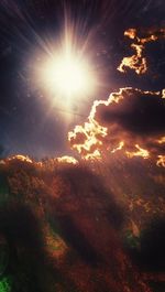 Low angle view of sun shining on mountain against cloudy sky