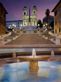 View of fountain by steps heading to built structure against sky at night