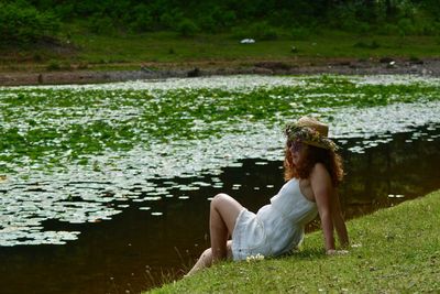 Side view of woman sitting on grass by lake