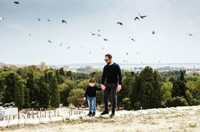 Father and son standing on footpath against birds