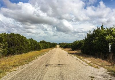 Dirt road by trees against sky